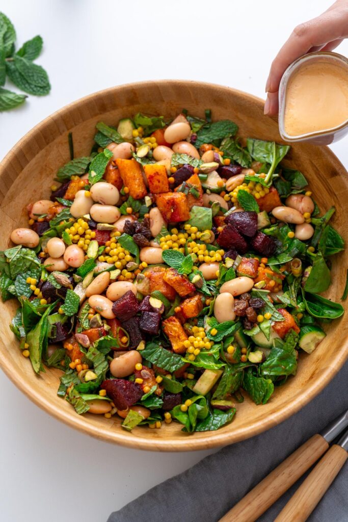 Sarah Cobacho holding a small jug of tahini dressing about to drizzle over Moroccan Spiced Pearl Couscous Salad.